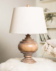 Wooden table lamp with beige linen shade on flurry table.