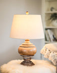 Wooden table lamp with beige linen shade switched on, on flurry table.