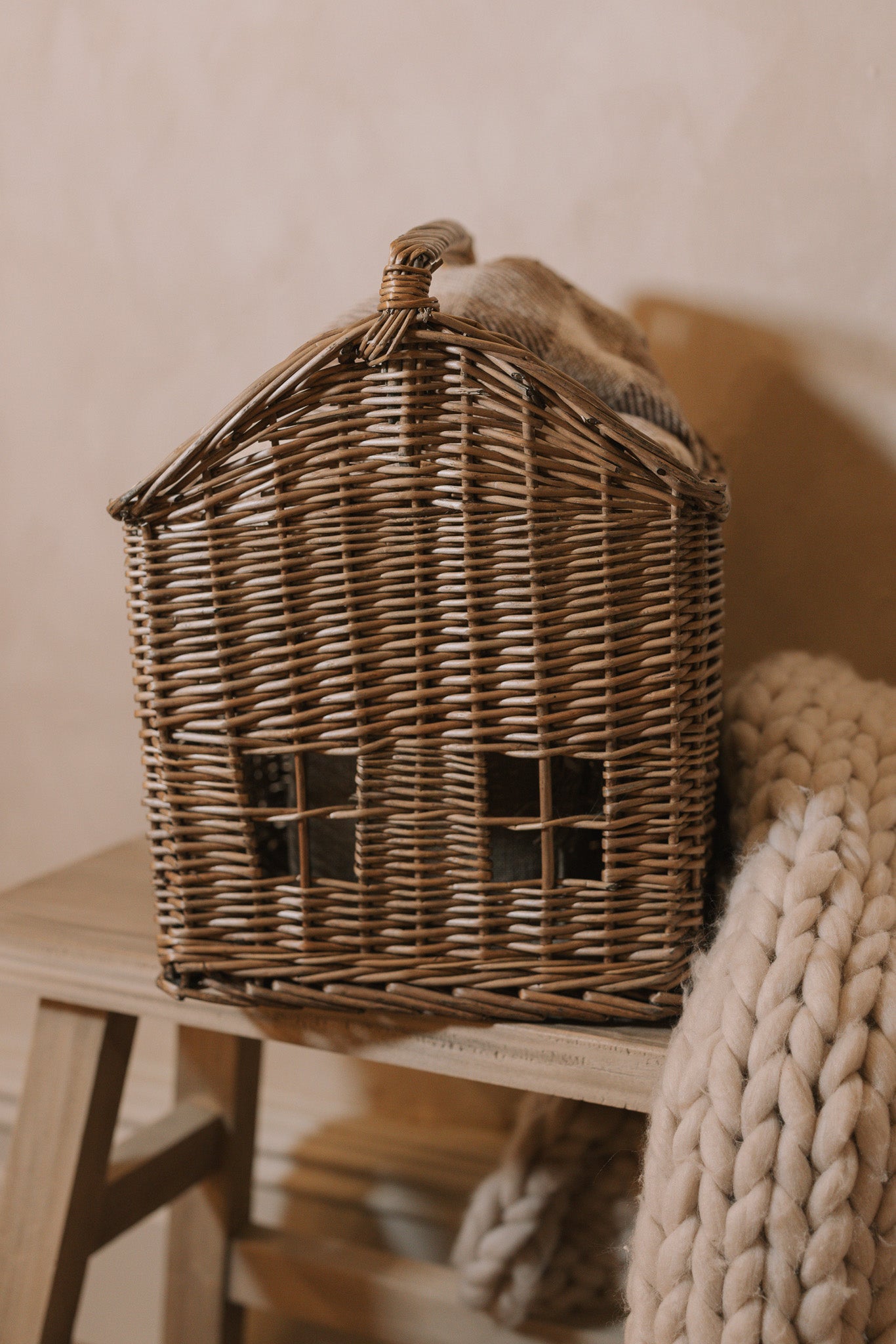 Woven basket with handle with chunky knitted throw on wooden bench.