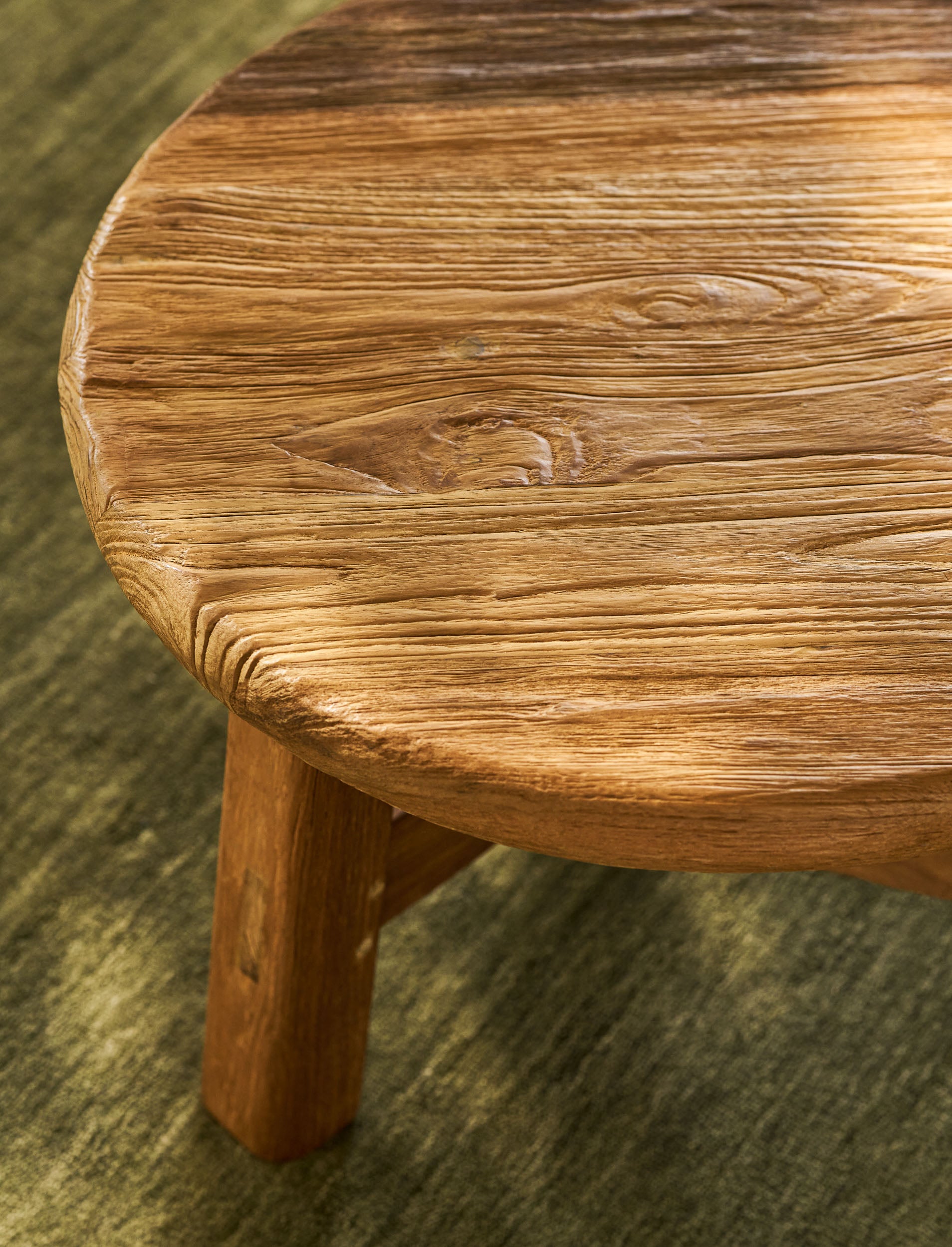 Close-up of a round wooden table with a textured surface on a green carpet.