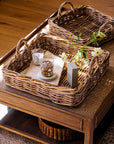 Natural woven trays on a wooden table with a glass of water and a bottle.