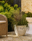Large outdoor planter with plant on a patio with wicker chair and brick wall in the background
