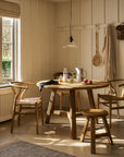 Wooden dining area with round wooden dining table and chairs in a well-lit room.