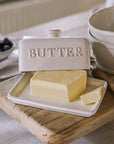 Ceramic butter dish with embossed 'butter' name, and block of butter on wooden serving board.
