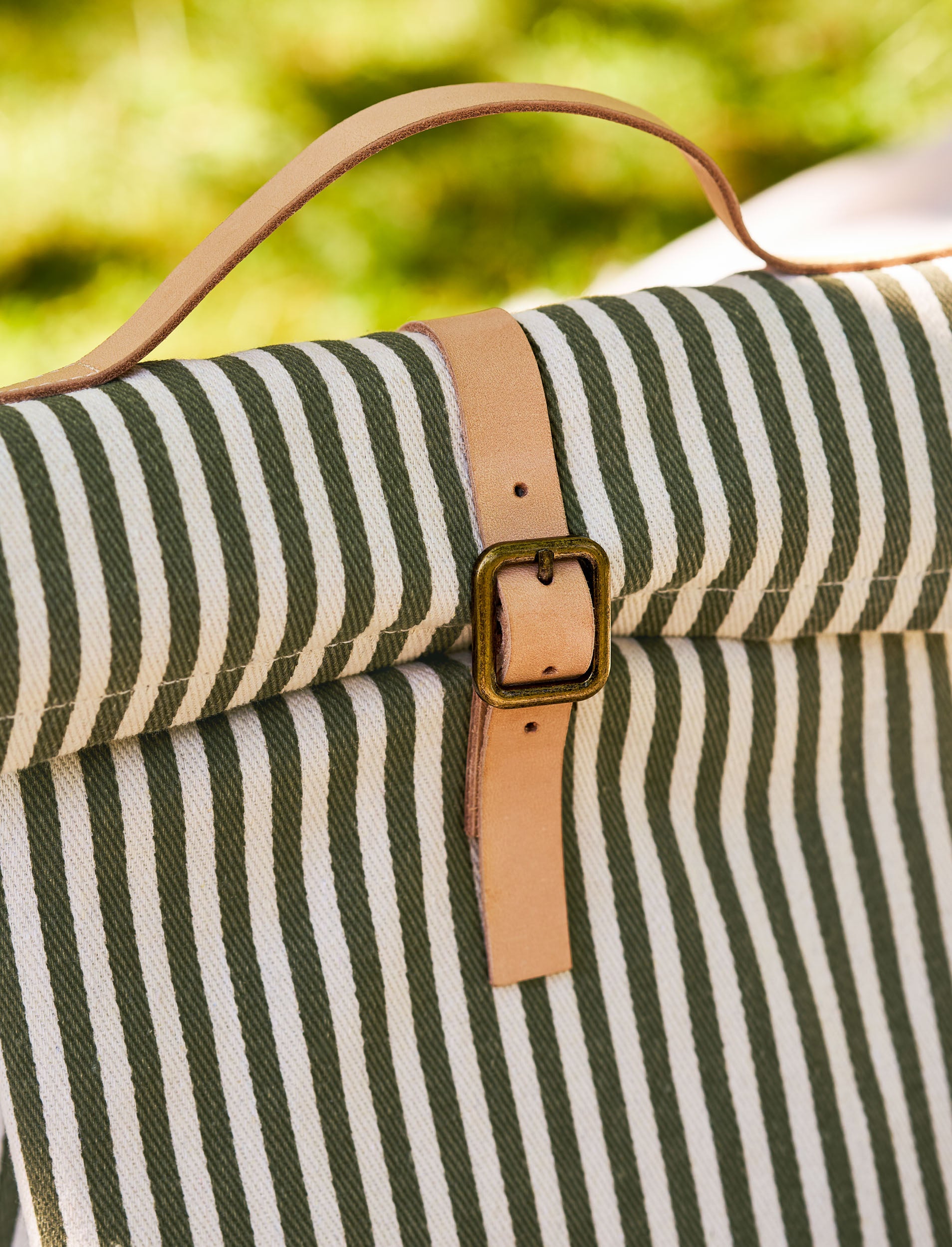 Striped lunch bag with a brown strap and buckle against a blurred green background