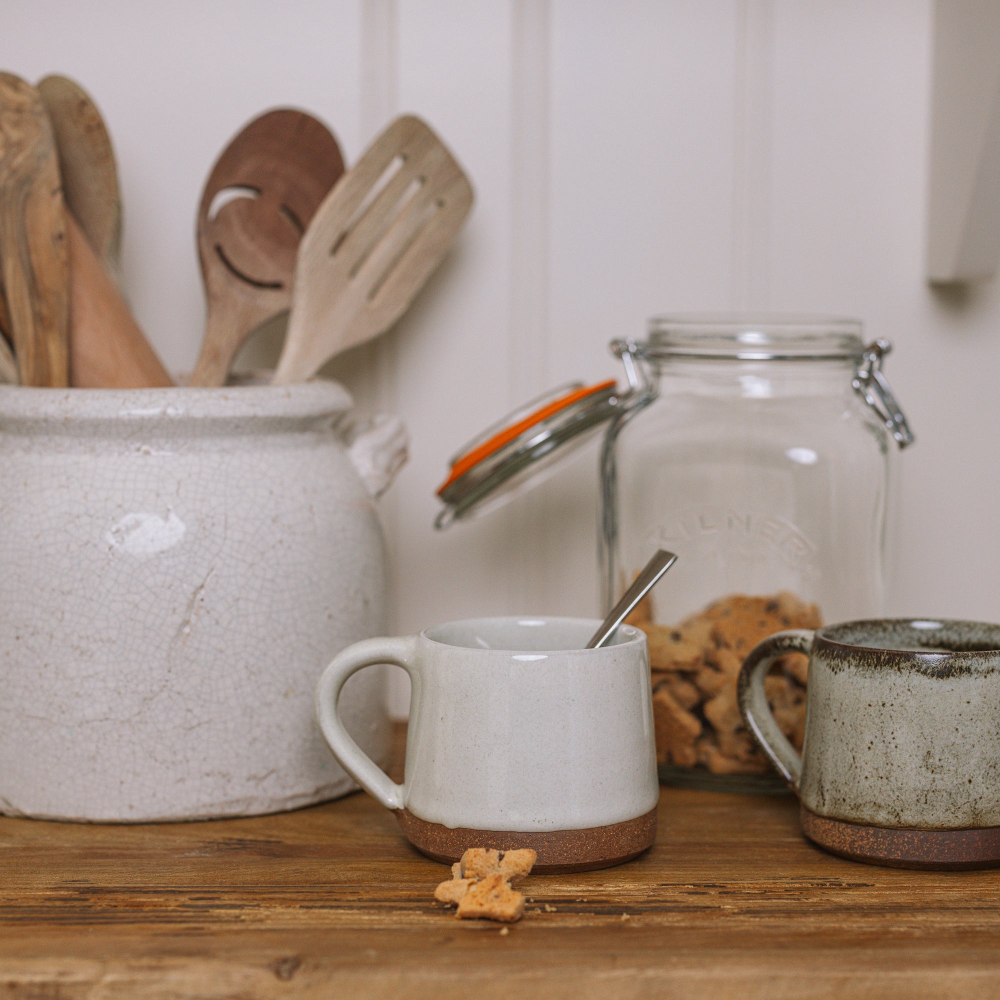 handmade milk white stoneware mug with stone base on wooden chopping board with crumbled biscuit.