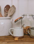 handmade milk white stoneware mug with stone base on wooden chopping board with crumbled biscuit.