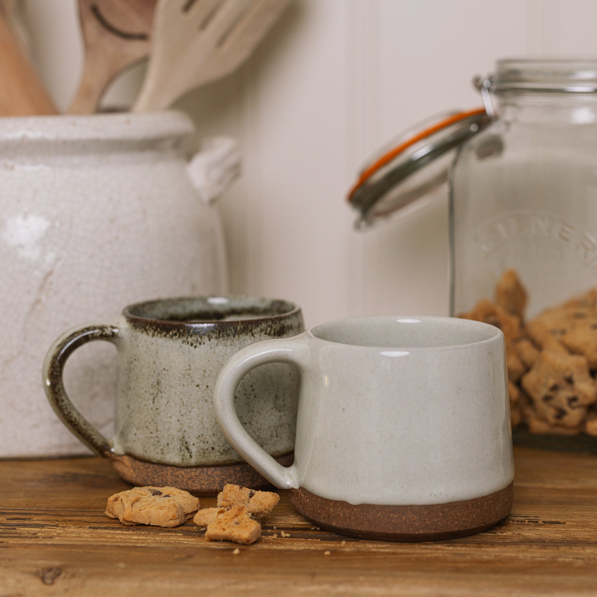 handmade milk white stoneware mug with stone base on wooden chopping board with crumbled biscuit.
