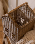 Woven basket with handle with chunky knitted throw on wooden bench.