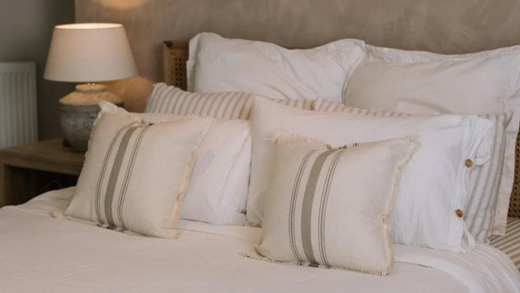 White cosy home bedspread with striped cushions and a table lamp.