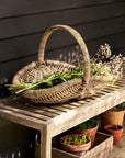 Rattan garden trug basket with greenery on a wooden bench against a dark wall