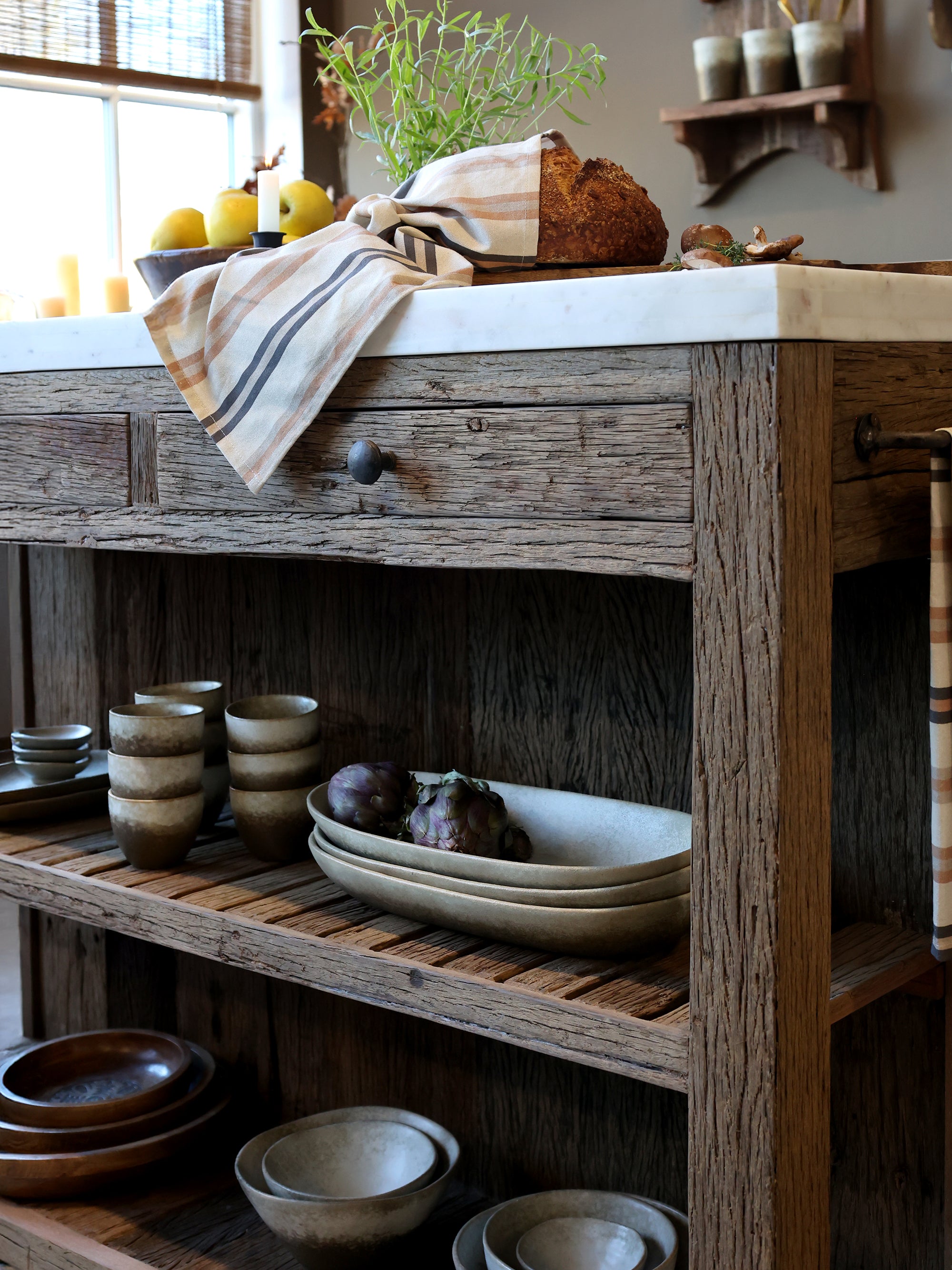 Wooden butchers block with marble top with rustic decor, including bowls and a loaf of bread.