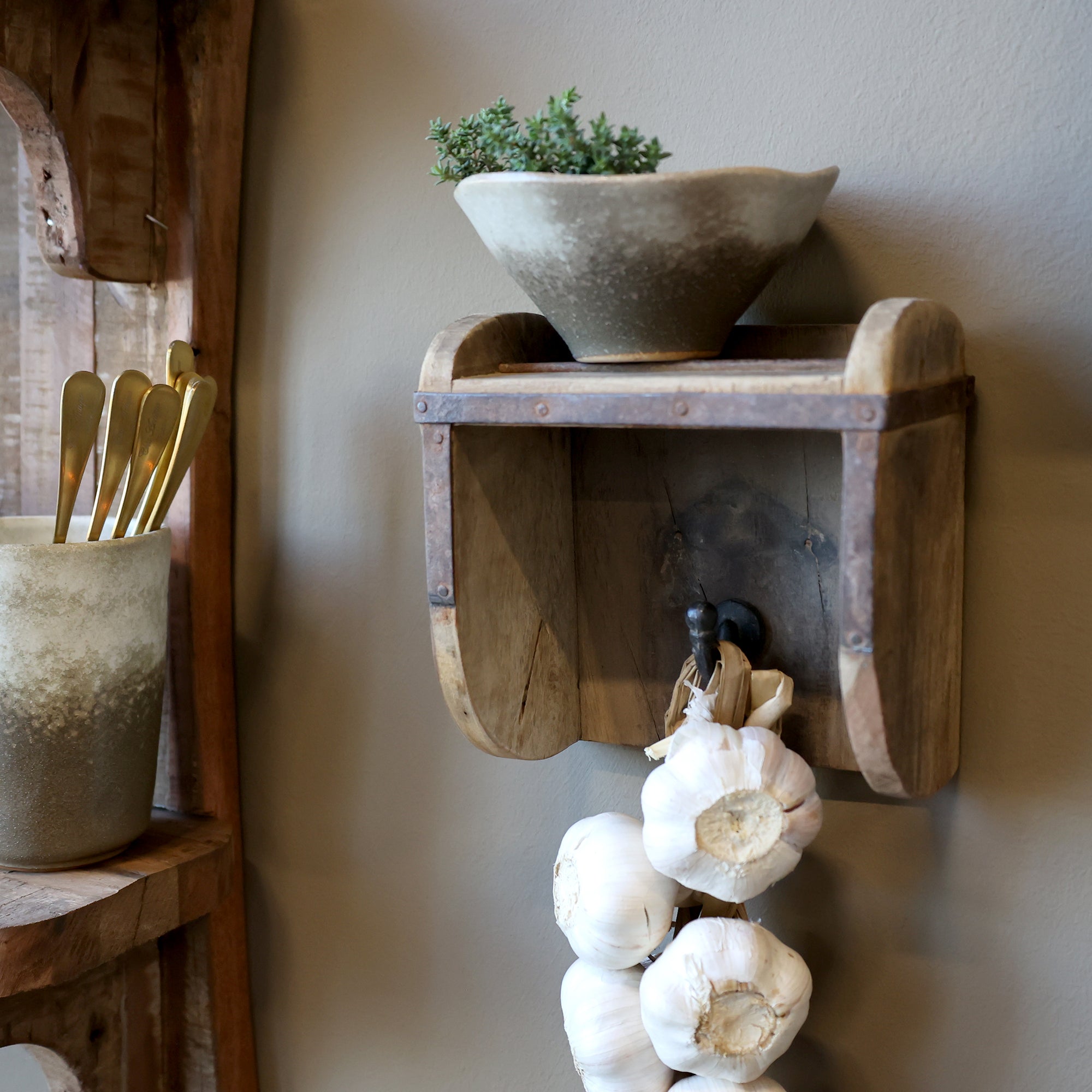 Wooden wall hook & shelf with a bowl, plant, and garlic hanging on a neutral wall.