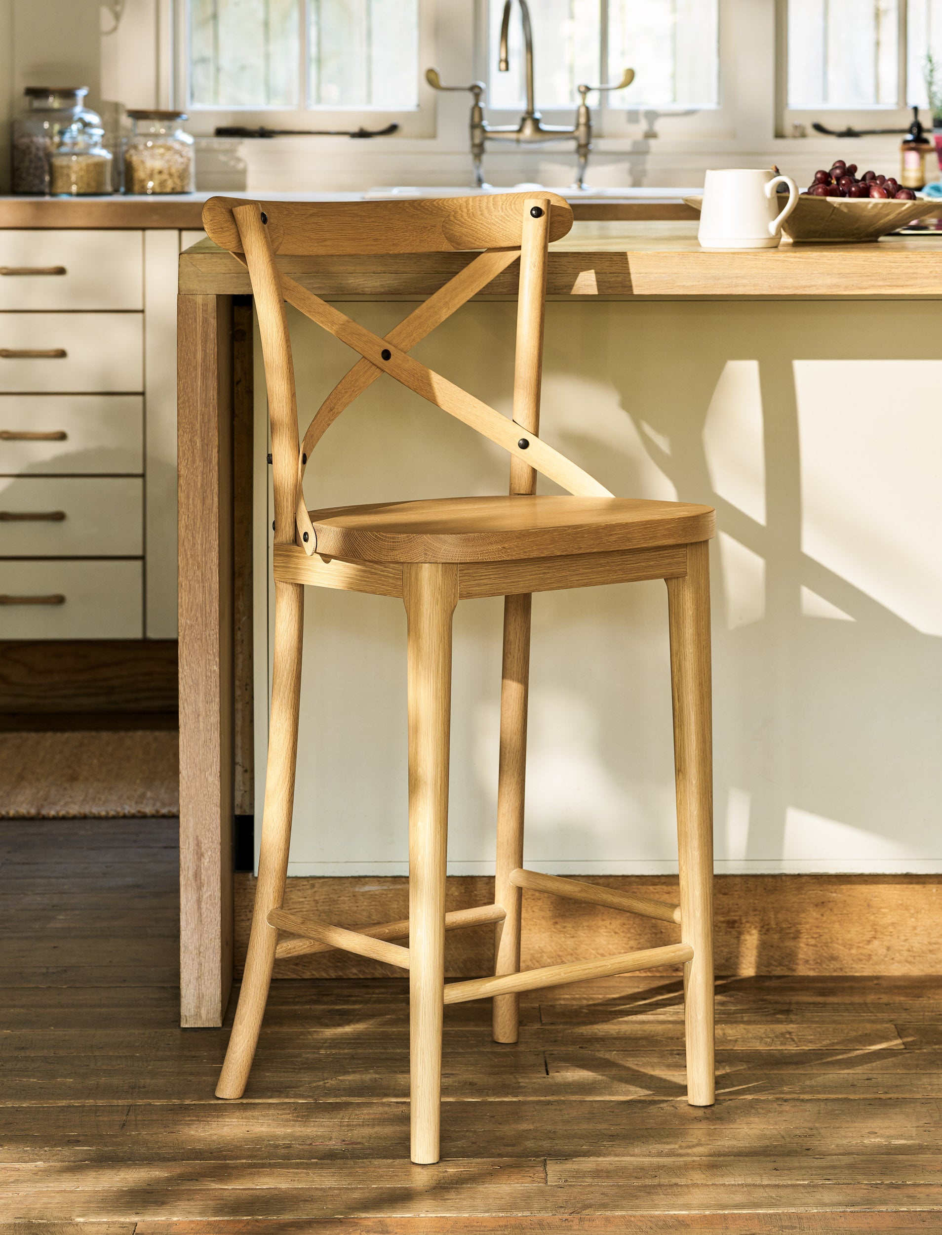 Wooden bar stool in a kitchen setting with a light-colored countertop and cabinets.