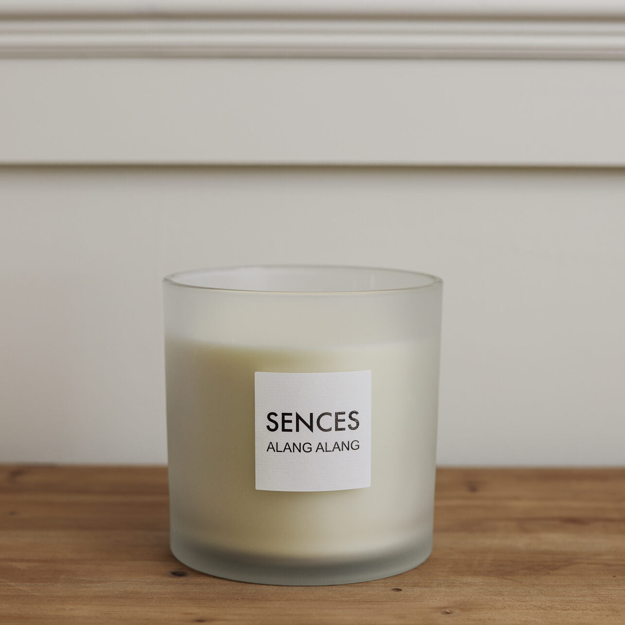 Sences Alang Alang White three wick candle in frosted glass on wooden table.