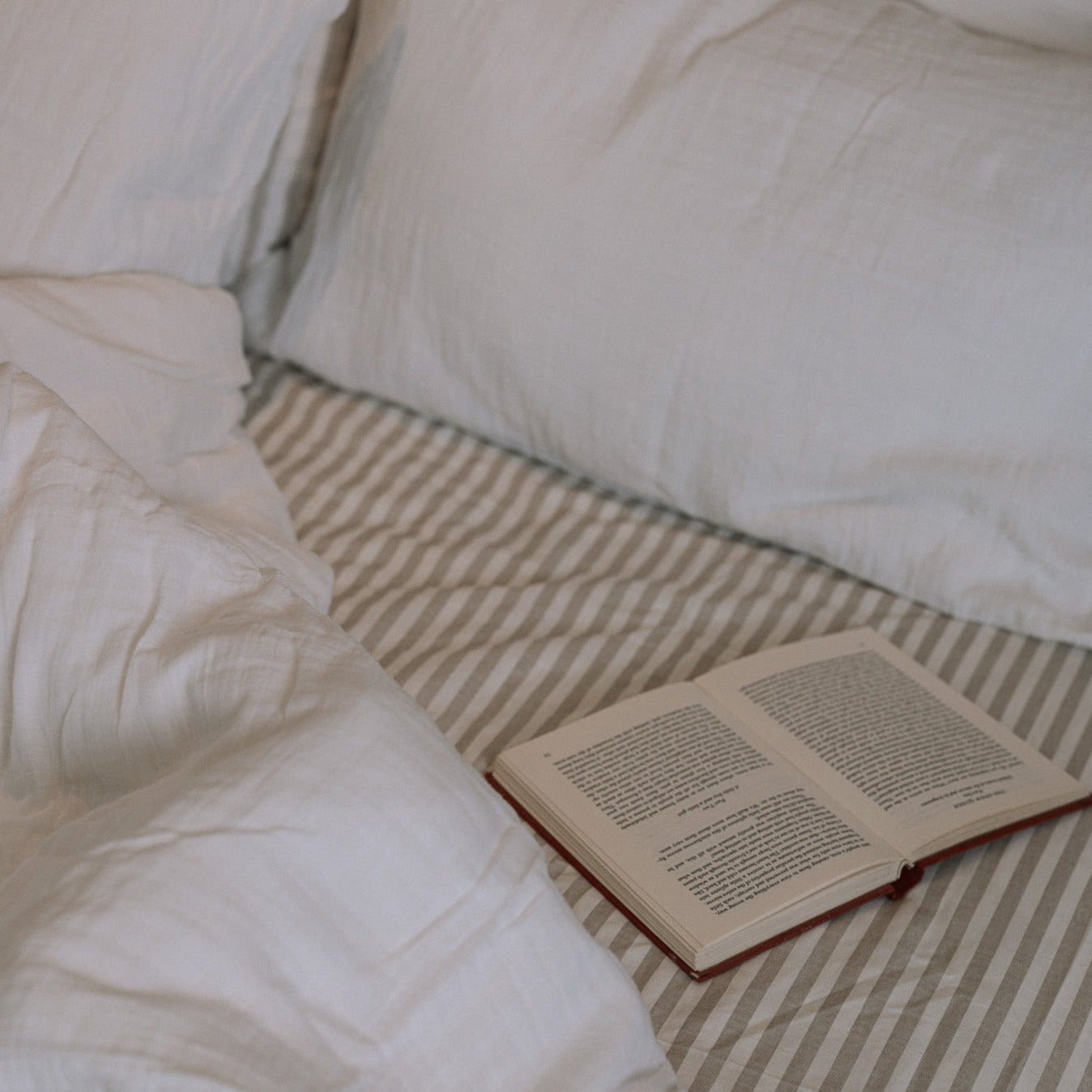 unmade white and striped bedding with an open book.
