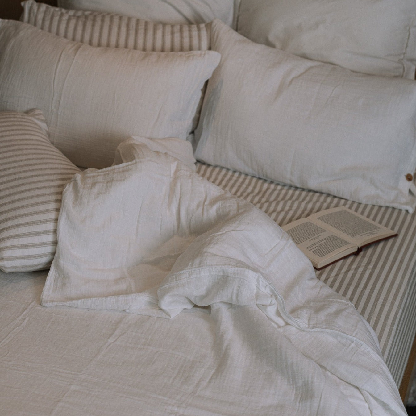 unmade white and striped bedding with an open book.