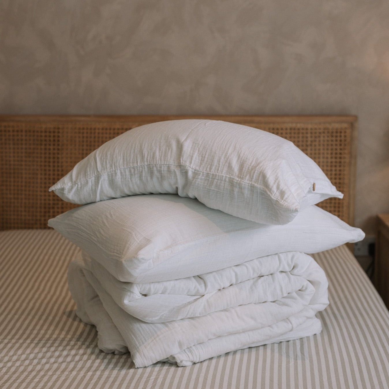 Folded white muslin bedding on striped bedsheet.