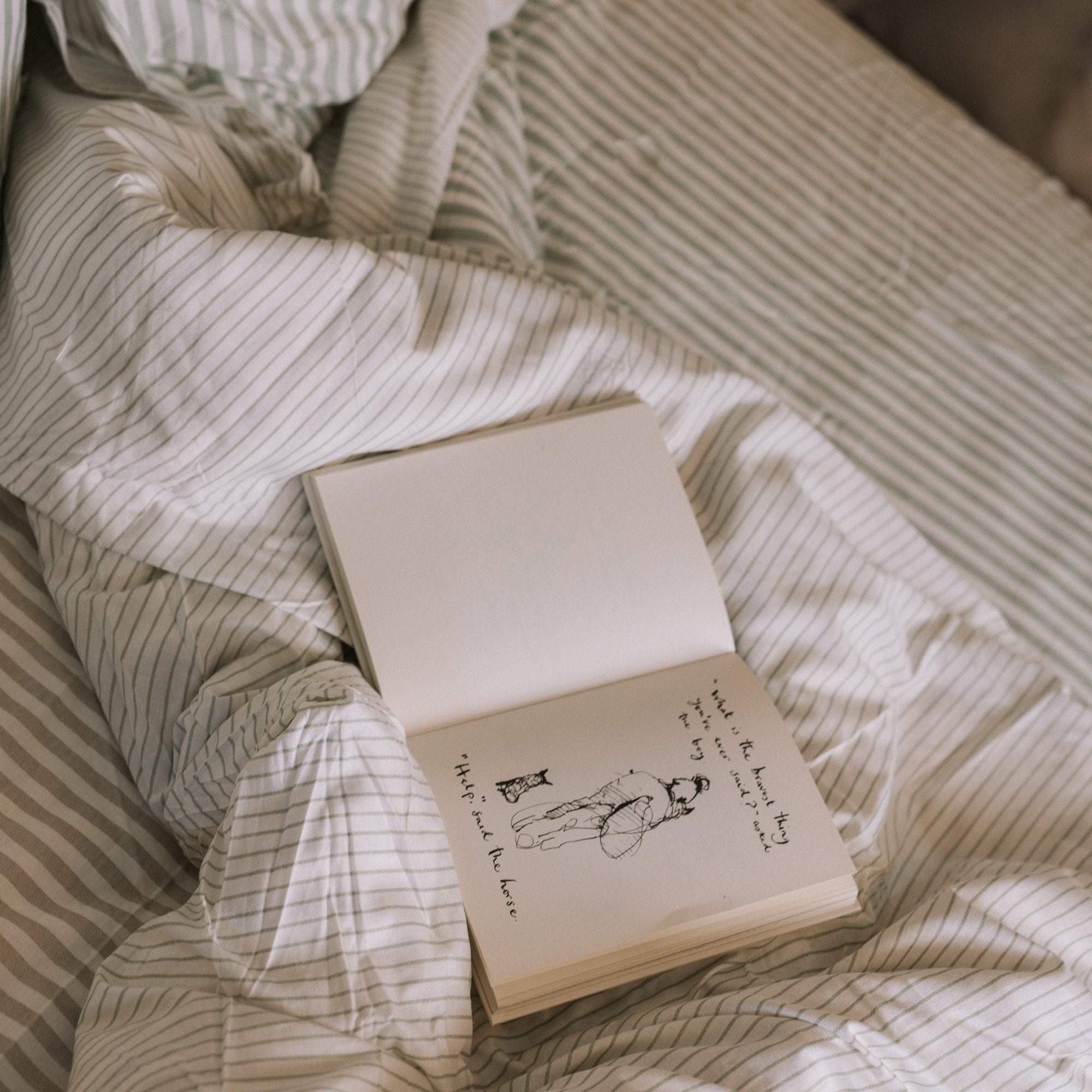 Green striped bedding, unmade with an open book.