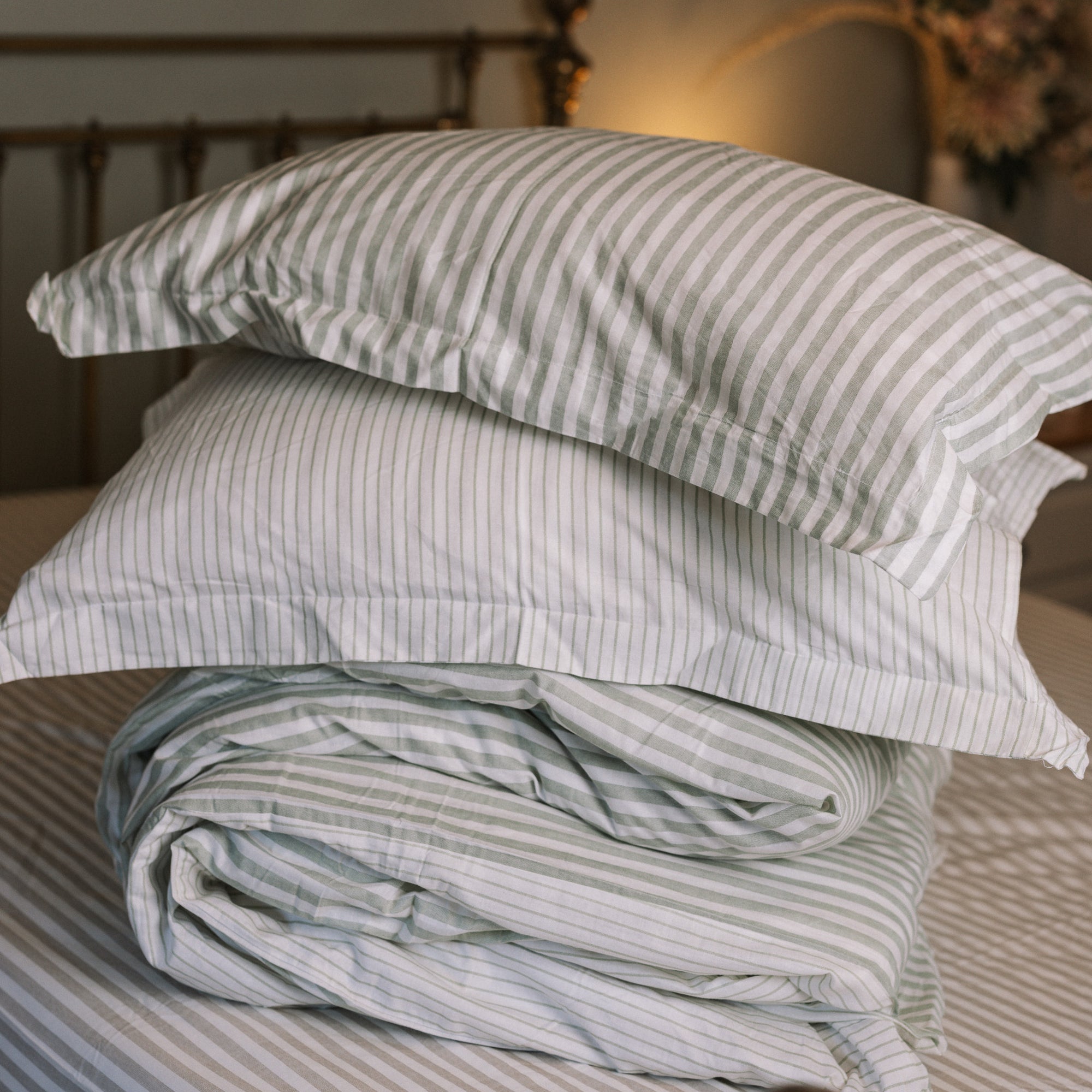 Green striped bedding folded up on a striped bedsheet.