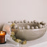 Grey ceramic bobble bowl with a lit candle and dried hops.