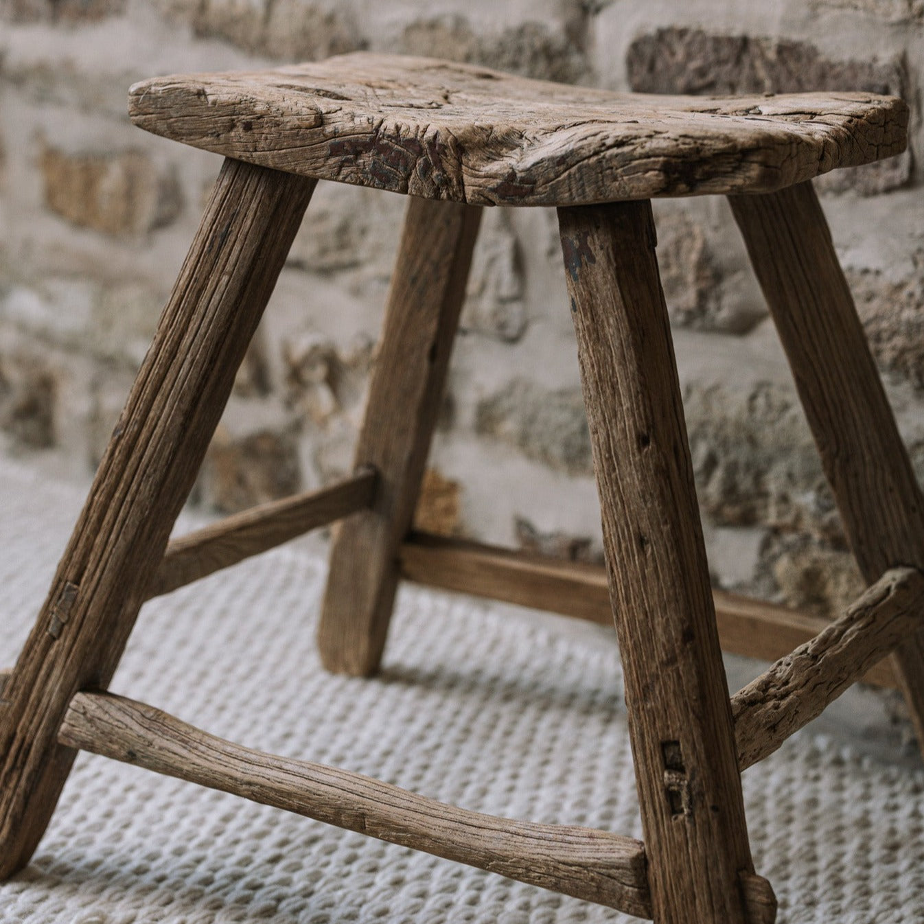 A reclaimed style wooden stool against a stone wall.