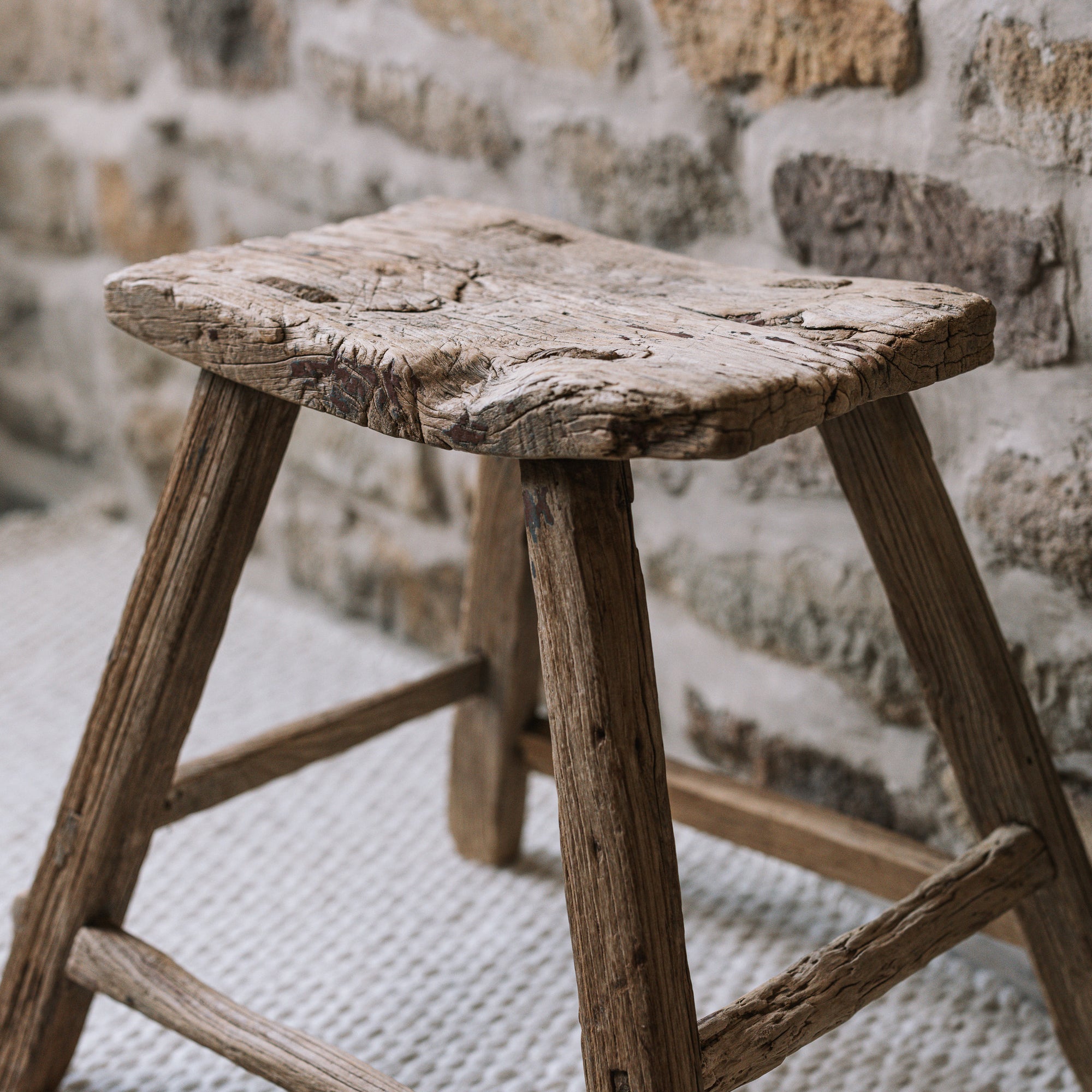 A reclaimed style wooden stool against a stone wall.