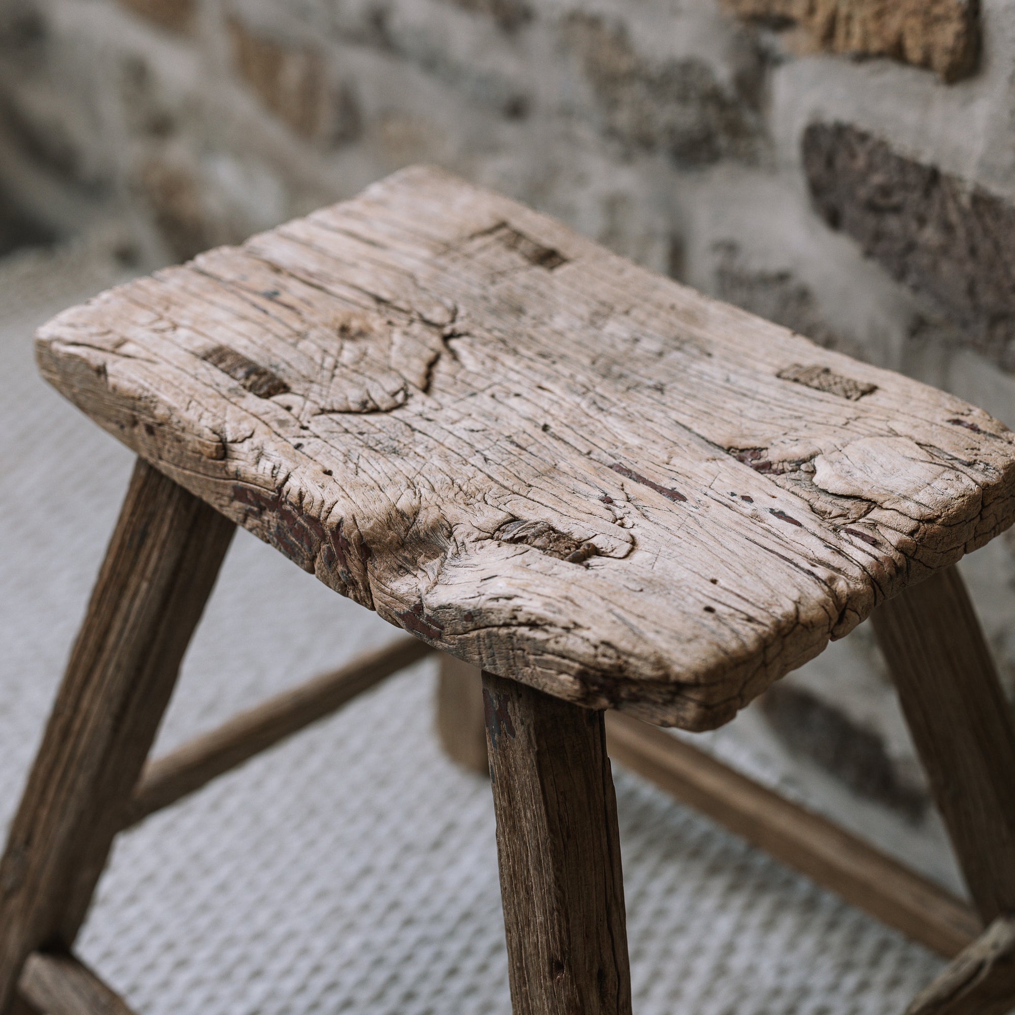 A reclaimed style wooden stool against a stone wall.