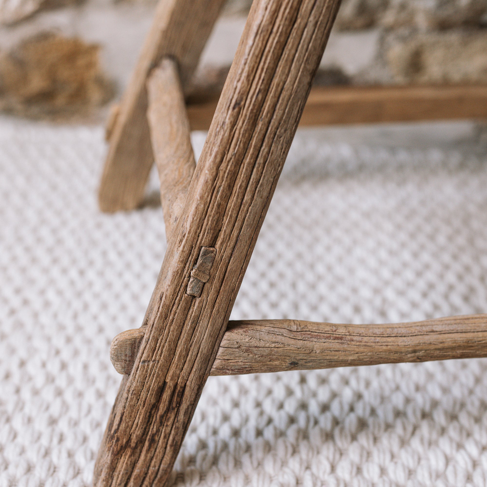 The leg of a reclaimed style wooden stool against a stone wall.