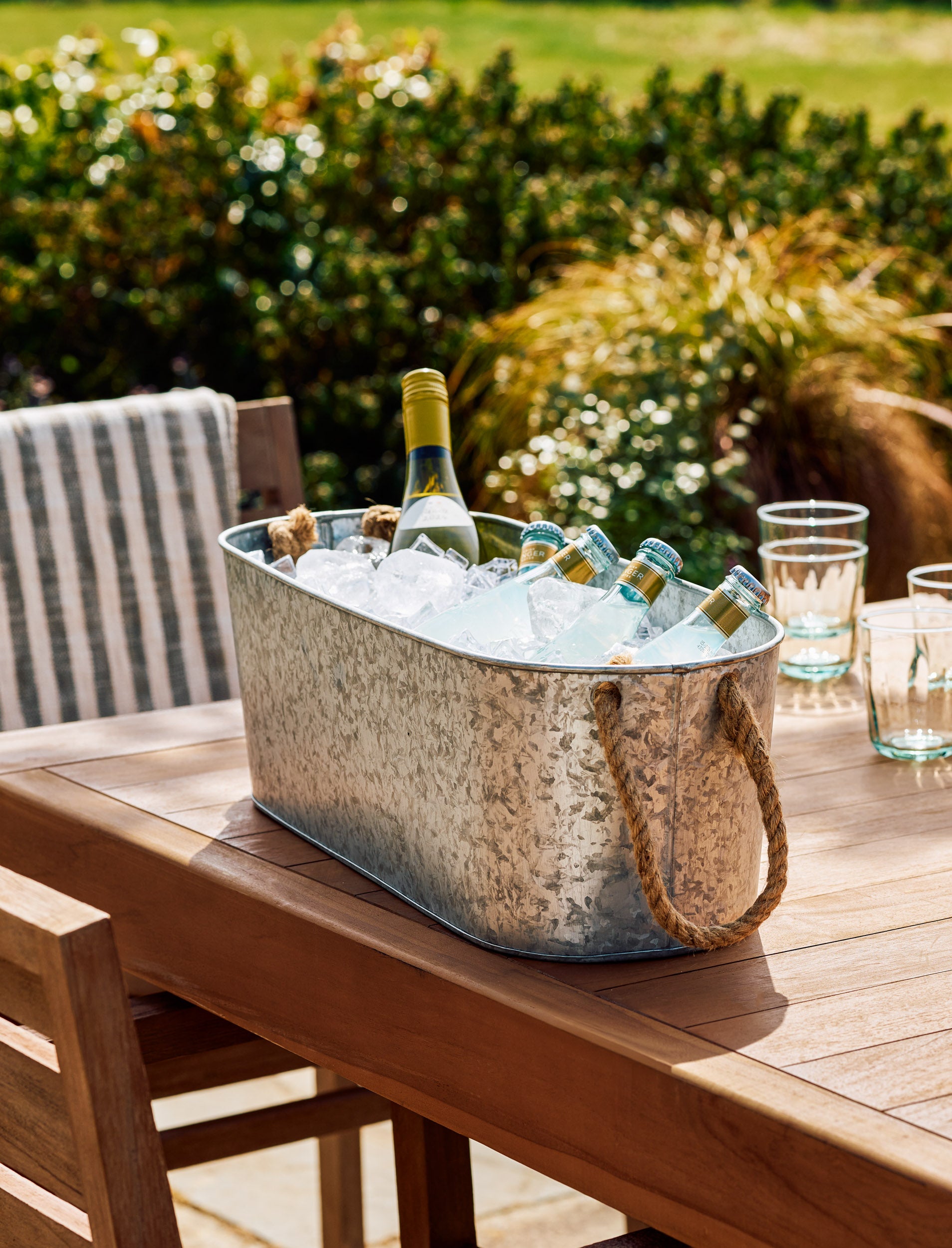 Metal ice drinks bucket with bottles of wine and water on a wooden table outdoors.