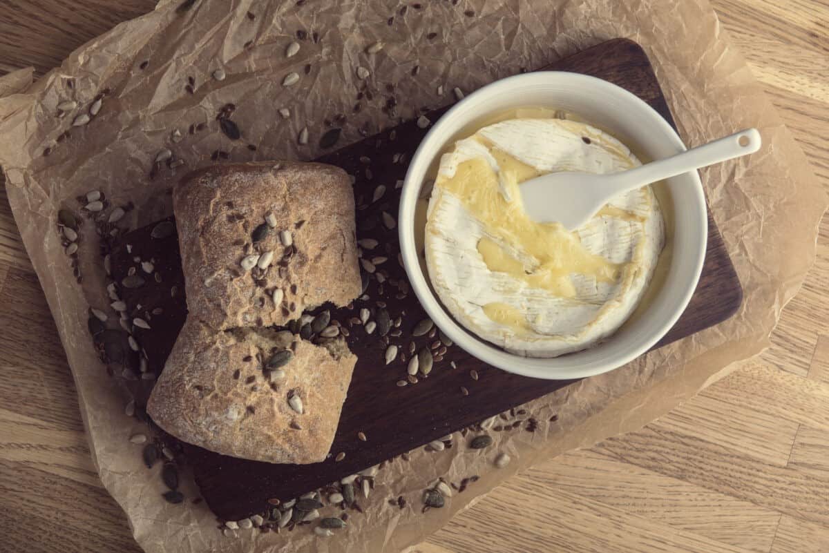  Stoneware Cheese Baker Set on wooden paddle with melted brie and crusty bread.