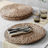 Set of 4 woven placemats, with three in a stack and one separately with napkins and cutlery.
