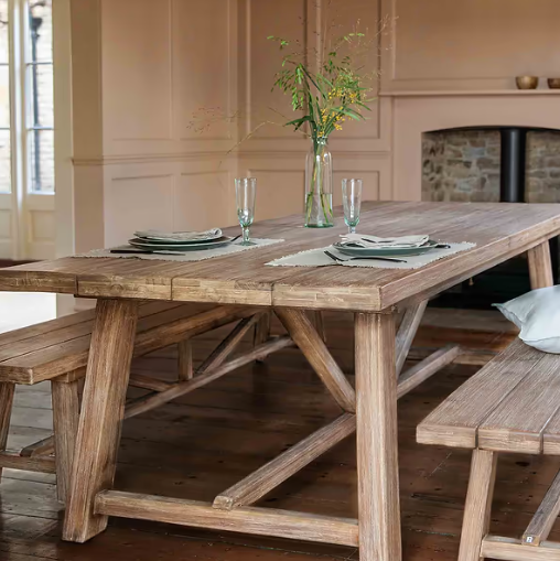 Large pine dining table in living room with dining benches and table settings for two.