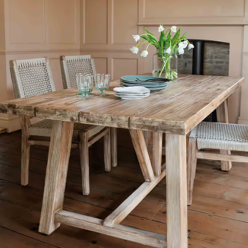 Small pine dining table with woven dining chairs in dining room, with plates, glasses, and a vase on the table.