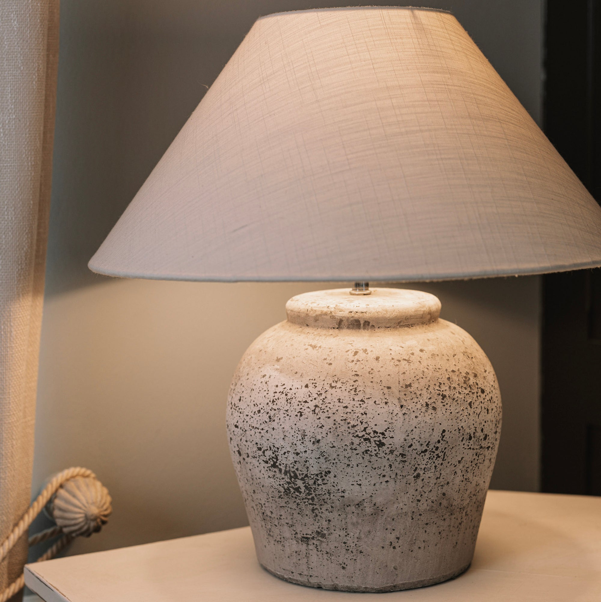 Antique grey lamp base with white lamp shade against a blue and black background. 