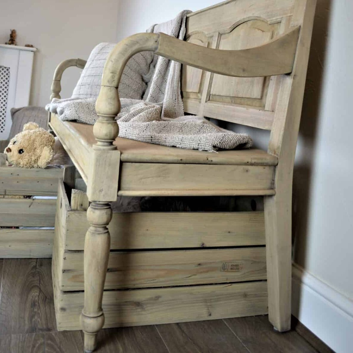 Vintage wooden bench with back with throw and cushion, and baskets underneath. Side view and close up of leg detailling.