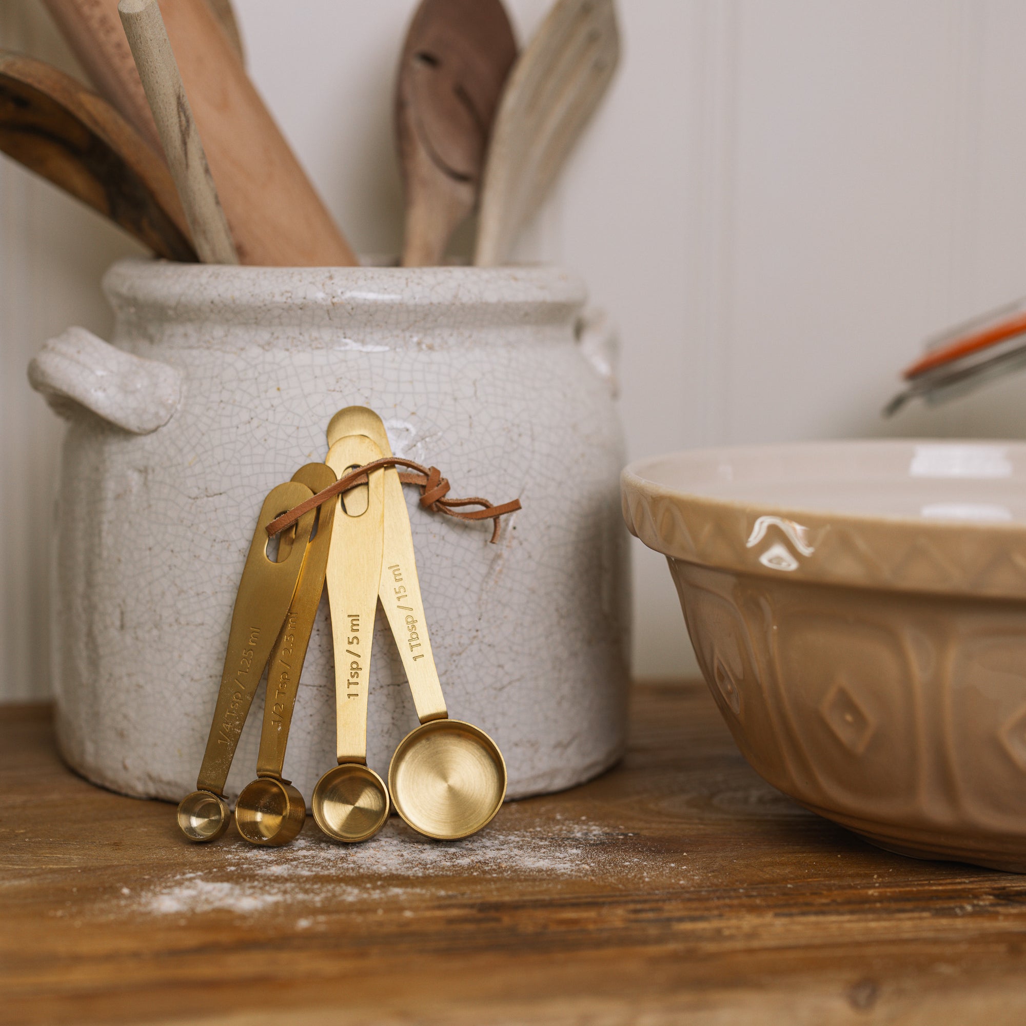 Brass Measuring Spoons on white ceramic utensil pot on bread board.