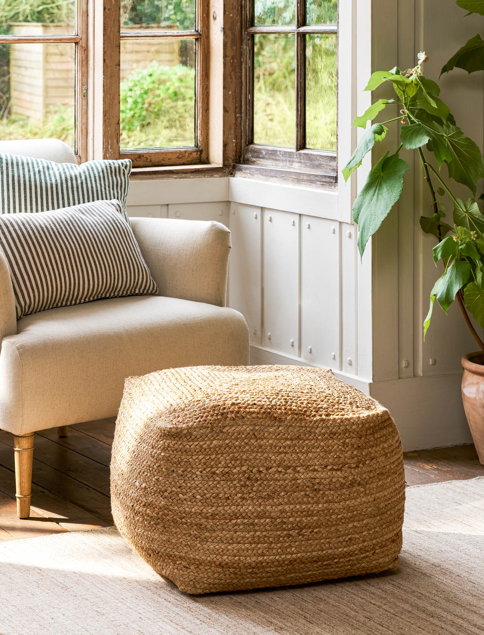 Square jute pouf in front of a cream armchair.
