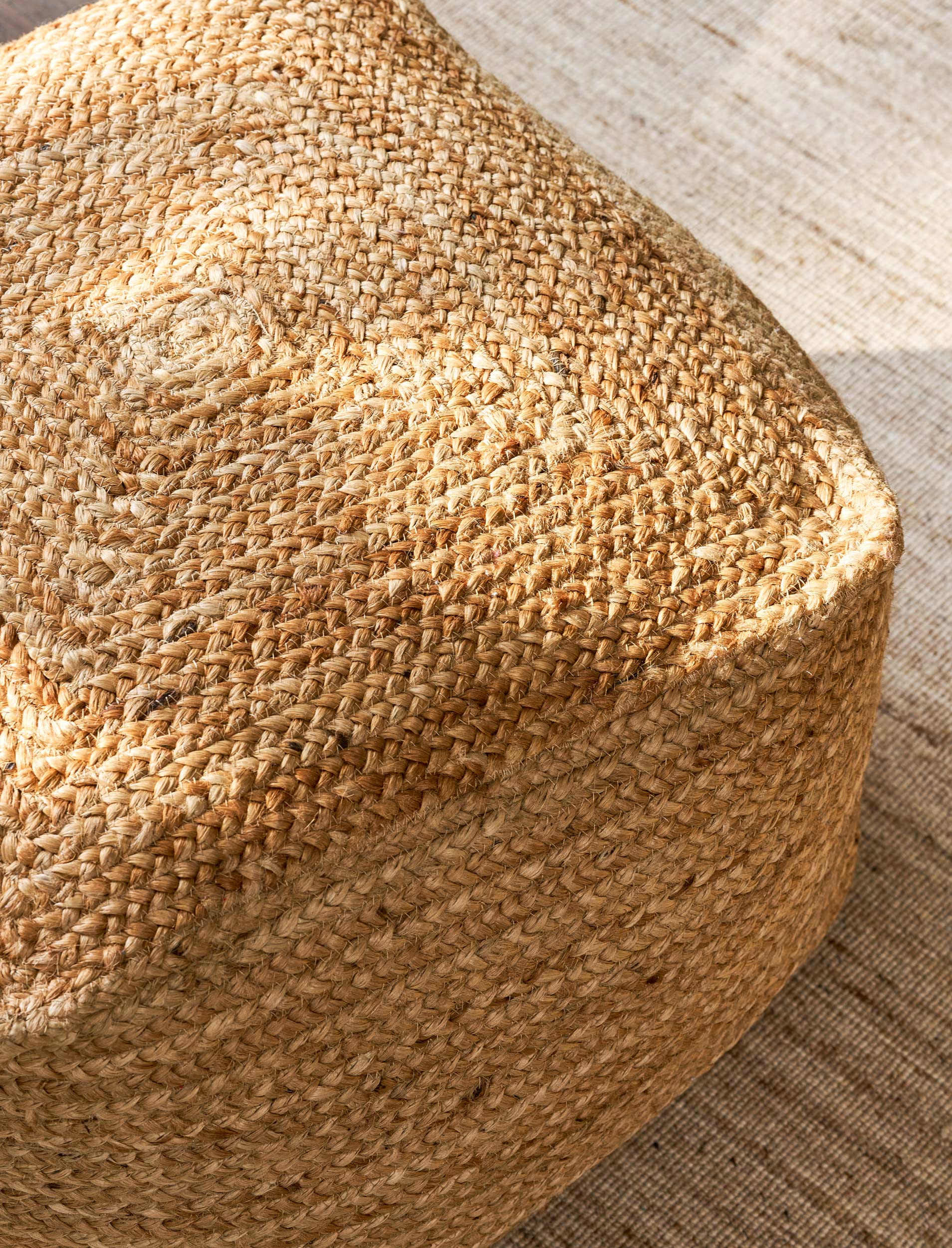 Close-up of a woven jute pouf on a wooden floor.