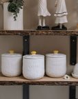 Daisy Tea coffee sugar canisters on wooden shelf with ceramic decorations