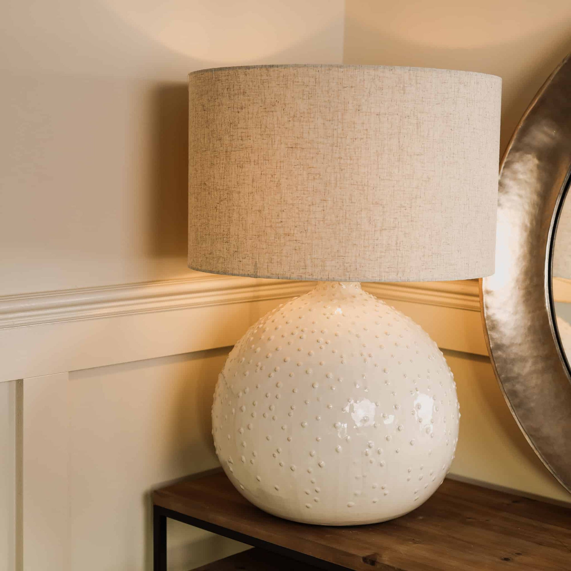 White dimpled light with linen lamp shade, switched on on wooden console. 