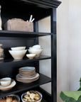 Close up of shelves filled with kitchen crockery and food on black shelving unit.