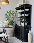 Black shelving unit filled with kitchen crockery in room with plants.
