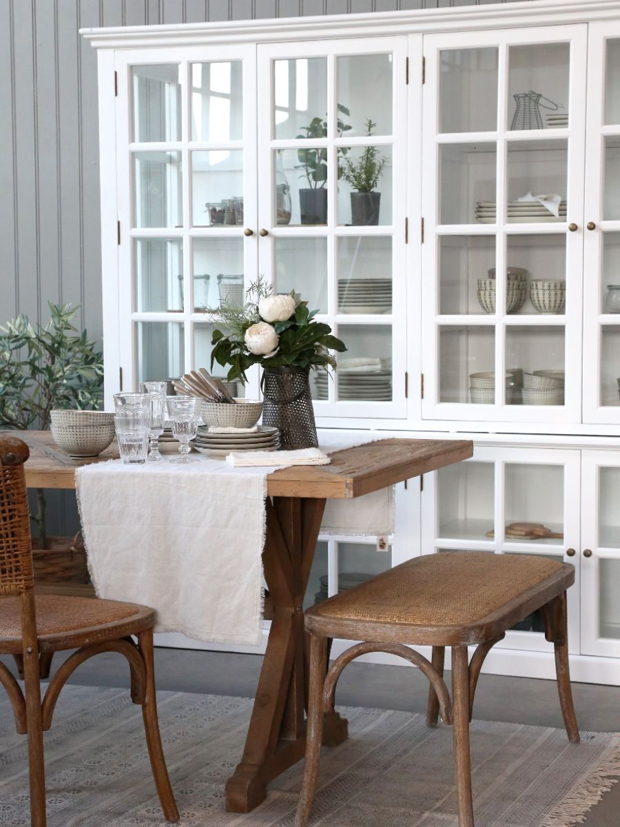Large white armoire cabinet with glass doors filled with kitchen crockery, next to a dining table.