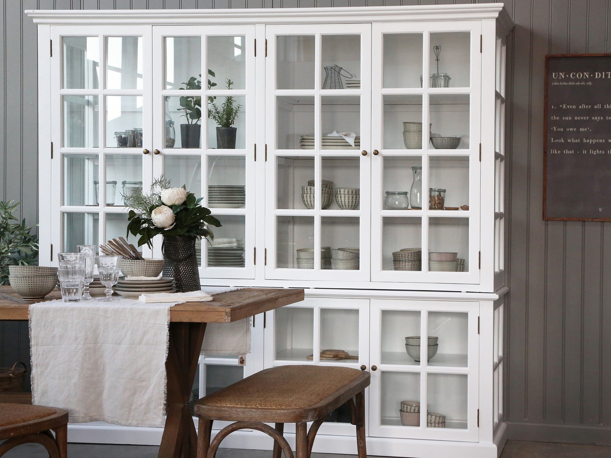 Large white armoire cabinet with glass doors filled with kitchen crockery, next to a dining table.
