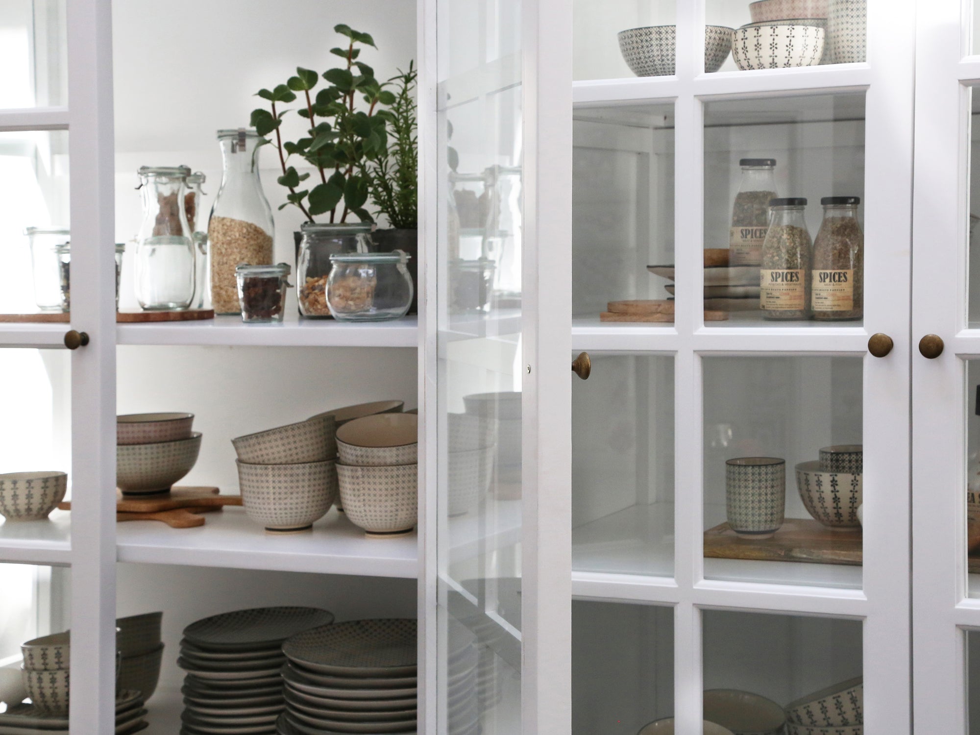 Close up of glass doors on large white armoire cabinet, filled with kitchen accessories.