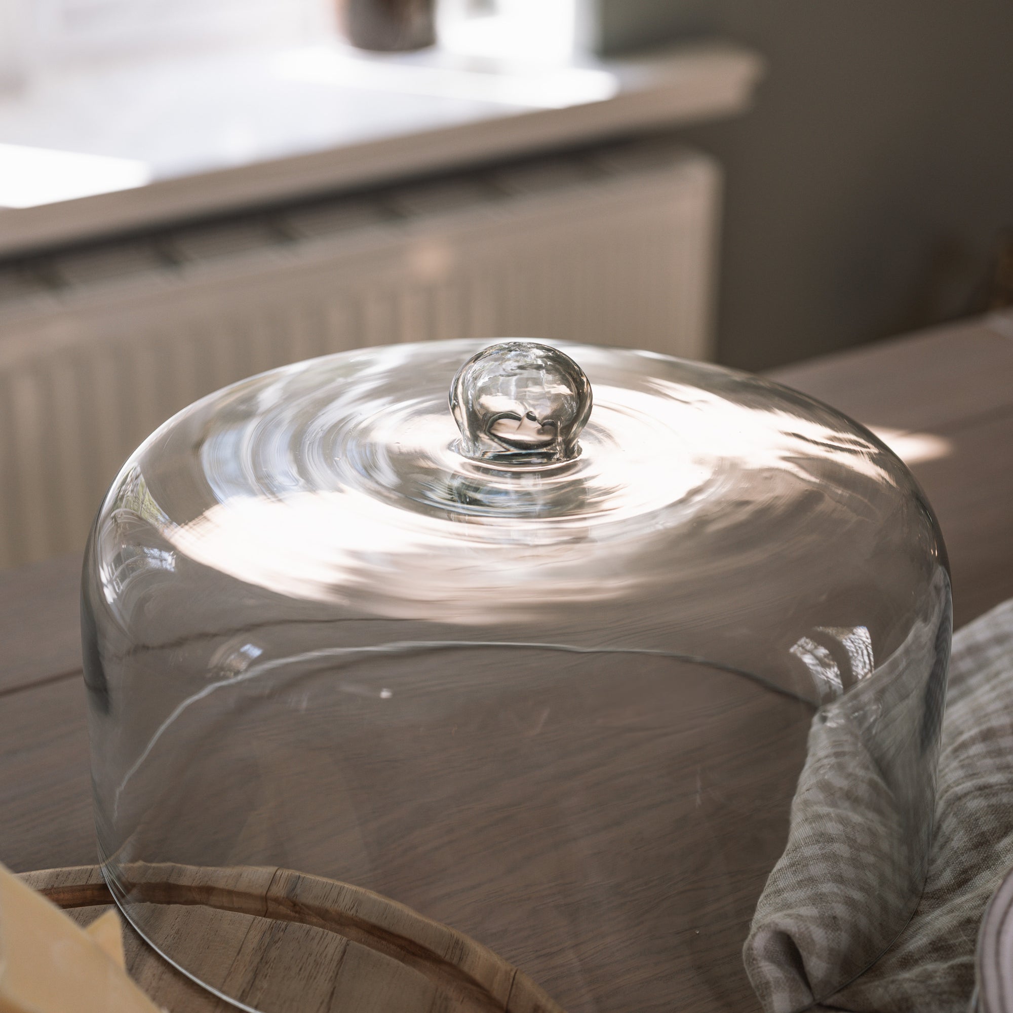 Glass cake dome cloche on wooden table with gingham tea towel.
