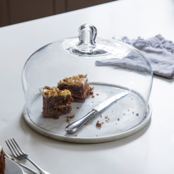 Marble and class cake dome with slice of cake and knife inside.