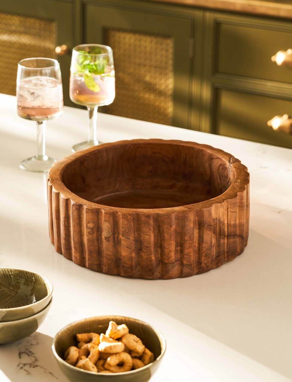 Wooden bowl on a kitchen counter with glasses and snacks