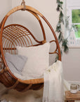 Natural rattan hanging chair for bedroom, with cushions and throw draped over.
